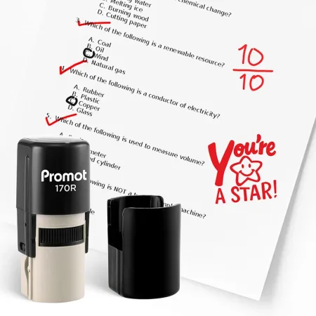 Black self inking stamp and removable cap displayed beside a graded science worksheet marked with red check marks, a “10/10” score, and a smiling star stamp that says “You’re A STAR!” The worksheet includes multiple choice science questions, and this ink