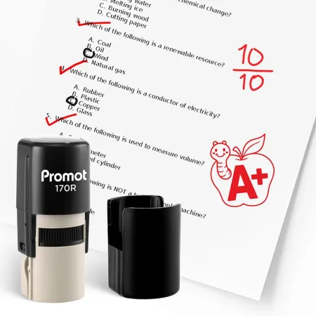 Black self inking teacher stamp and removable cap displayed beside a graded science worksheet marked with red check marks and a “10/10” score. A red apple stamp with a worm and “A+” design appears on the page, showing how the classroom stamp can reward ex