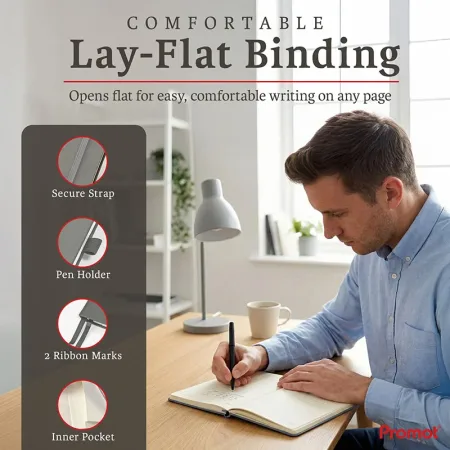Man writing in an open notebook at a desk, a personalized leather journal with lay-flat binding and built-in accessories.