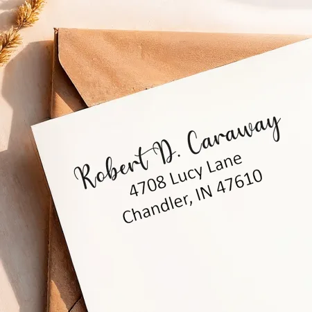 A clean return address from a small self-inking address stamp printed on a white envelope over a kraft envelope.