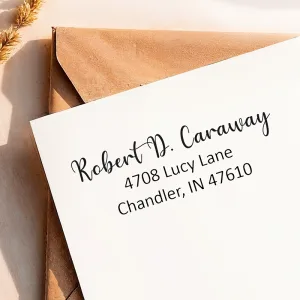 A clean return address from a small self-inking address stamp printed on a white envelope over a kraft envelope.