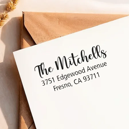 A crisp return address from a large self-inking address stamp printed neatly on a white envelope over a kraft envelope.