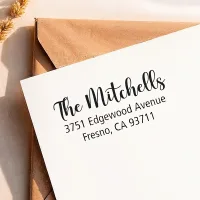 A crisp return address from a large self-inking address stamp printed neatly on a white envelope over a kraft envelope.