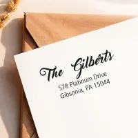 White envelope stamped with "The Gilberts" return address above a kraft envelope using a custom address stamp.