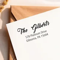 Custom address stamp impression with a scripted return address on a white envelope over a kraft envelope.